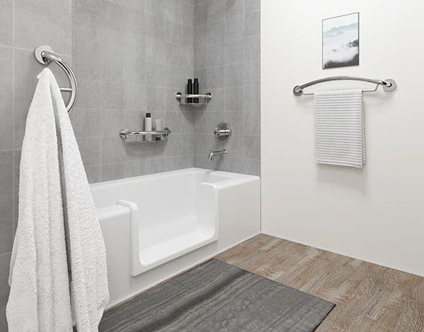 Modern accessible bathroom with white walk-in tub, gray tile walls, chrome grab bars, towel racks, and wood-look flooring