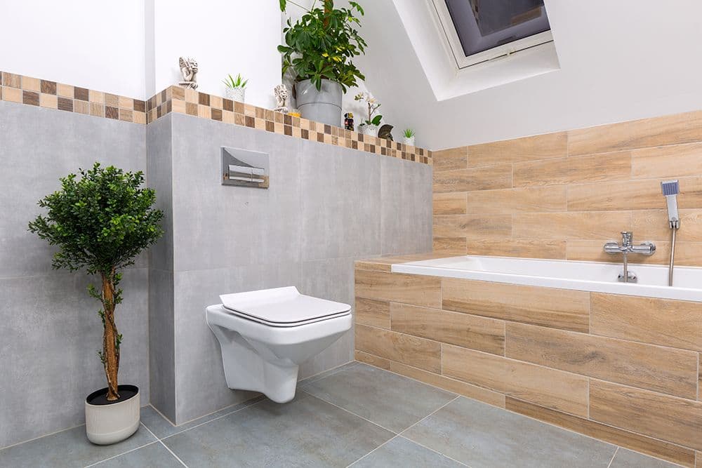 Modern bathroom with wall-mounted white toilet, wooden tile accent wall with built-in bathtub, gray concrete tiles, decorative plants, and skylight window