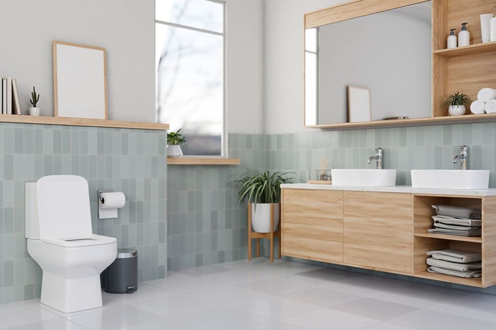Modern bathroom with white toilet, dual white vessel sinks, wooden vanity with storage, mint green tile backsplash, wooden mirrors and shelves, potted plants, and natural light from window